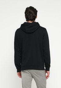 Svart luvtröja med ledig passform, långärmad och med ribbade muddar. Mjukt material. Ljusgrå randiga byxor syns längst ner.