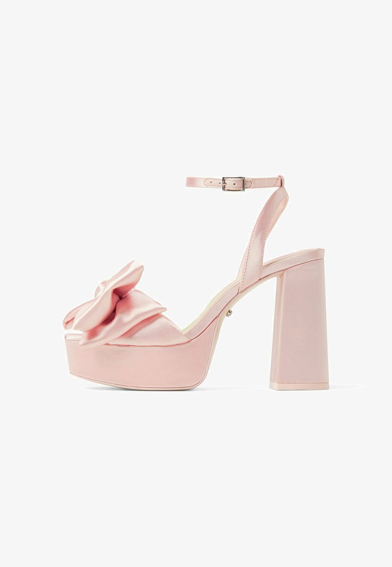 Pink satin platform sandals featuring a large bow detail, ankle strap with buckle, and a square block heel. Smooth texture and glossy finish.