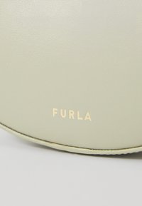 Furla torbica od svjetlozelene teksturirane kože, s glatkom površinom i ugraviranim zlatnim logotipom na donjem rubu. Okrugli oblik.