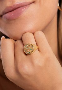 Anillo de oro con una parte superior redonda, que presenta varias piedras preciosas de colores dispuestas en un patrón de cuadrícula. Textura suave y acabado pulido.