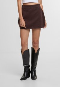 Brauner Strick-Minirock mit einem gerippten Bund und einer ausgestellten Form. Kombiniert mit hohen schwarzen Lederstiefeln mit spitzen Zehen.