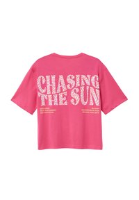 Roze oversized t-shirt met korte mouwen. Bevat een witte grafische opdruk met de tekst "CHASING THE SUN" en aanvullende tekst eronder.
