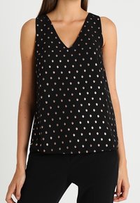 Top senza maniche nero con scollo a V profondo e pois metallici color oro rosa, realizzato in un tessuto morbido che cade morbido.