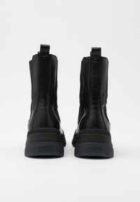 Botas de tobillo negras hechas de cuero suave con una suela de goma texturizada. Cuentan con una lengüeta y paneles elásticos en los laterales para facilitar su uso.