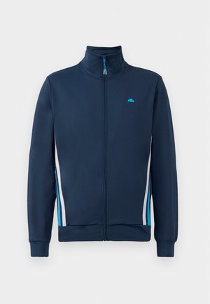 Marine-blå zip-jakke med høj krave, udstyret med hvide og lyseblå sidestreger samt et lille logo på brystet. Glat tekstur og tætsiddende design.