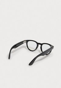 Occhiali da sole neri a forma di gatto con lenti trasparenti, finitura lucida e bracci neri robusti con dettagli del logo discreti.