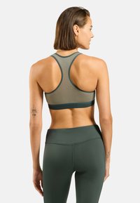 Soutien-gorge de sport en vert olive, présentant un design en maille texturée, une forme dos nageur et une large bande. Associé à un legging taille haute assorti.