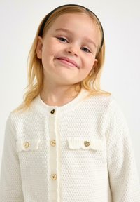 Witte gebreide cardigan met een textuurpatroon, ronde halslijn, knoopsluiting en hartvormige accenten op de zakken.