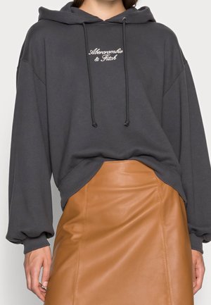 Sweat à capuche gris foncé Abercrombie & Fitch avec cordons assorti à une jupe en cuir camel taille haute portée par une personne.
