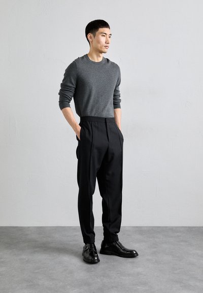 Suéter gris, pantalones negros de cintura elástica y zapatos negros brillantes. El conjunto presenta un corte relajado y líneas limpias, sin patrones visibles.