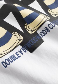 Fehér pamut póló, amelyen kék és bézs csíkos közlekedési kúpok ismétlődő grafikája látható, alatta a „DOUBLE A BY WOOD WOOD®” felirattal.