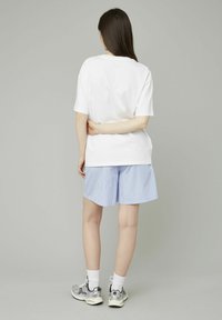 T-shirt en coton blanche à manches courtes, associée à un short rayé bleu clair. Le modèle porte des baskets argentées et des chaussettes blanches.