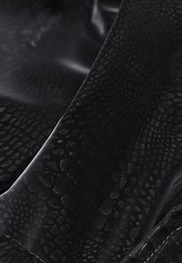 Must tekstureeritud kangas, millel on peen roomaja meenutav muster ja pehmed, siledad voldid lähivaates.