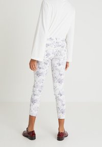 Vita byxmönstrade ankelnederdelar med lila och grå blommor, figurnära passform, blandning av bomullstyg, ihopkopplade med en långärmad vit top och bruna skor.