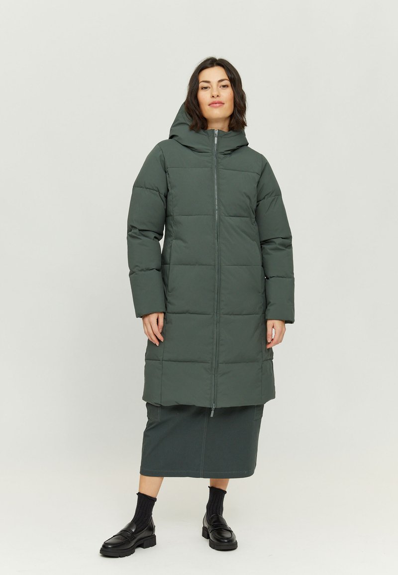 Long puffer coat in dark green, featuring a hood, front zipper, and quilted design. Paired with a matching skirt and black footwear.