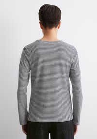 Schwarz-weiß gestreiftes Langarmshirt mit rundem Ausschnitt, aus einem weichen Stoff gefertigt. Verfügbar mit seitlichen Schlitzen am Saum für zusätzliche Details.