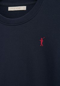 Marineblauw shirt met ronde hals met een kleine rood geborduurde figuur die een polo mallet draagt op de linkerborst en een "POLO CLUB" label in maat small in de kraag.