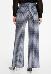 Pantalon large en motif pied-de-poule bleu et blanc, avec une taille haute et une texture subtile. Fini avec des talons hauts pointus et élégants.