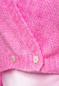 Chlupatý růžový kardigan s texturovaným pleteným designem, oboustranným zavinutím a dvěma světlými knoflíky jako akcenty.