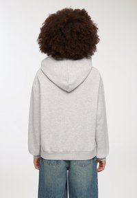 Felpa grigia in morbido tessuto, con cappuccio regolabile, maniche lunghe e orlo a coste, abbinata a jeans in denim a vestibilità ampia.