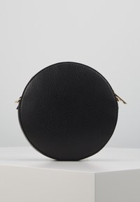 Borsa rotonda nera in pelle texturizzata. Presenta una cerniera dorata e una forma circolare, con una superficie liscia e un design compatto.