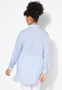 Camisetta a maniche lunghe a righe blu e bianche con colletto e polsini abbottonati, realizzata in un tessuto leggero e caratterizzata da una vestibilità rilassata.