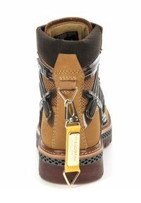Bota de senderismo marrón y negra con material de malla y cuero, que presenta una etiqueta de metal, un acento amarillo y una suela de goma texturizada con una base con patrón.