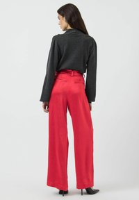 Pantalons larges en satin rouge avec une taille haute, des poches arrière et une texture lisse, associés à un top noir ajusté à manches longues.