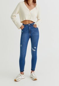 Vit ribbad kort tröja med V-ringning, i kombination med högmidjade blå skinny jeans med slitna detaljer och en slät yta.