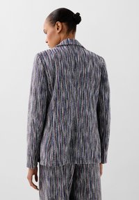Texturovaný blazer s vertikálními barevnými pruhy v purpurové, modré a stříbrné. Má klasický límec a dlouhé rukávy.