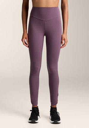 Magas derekú, sima textúrájú, lila leggings, amelyek tapered lábformával és bokarésszel rendelkeznek. Fekete sportcipővel párosítva.