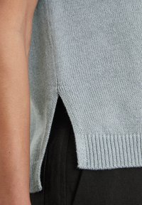 Helleblaue Strickjacke mit seitlichem Schlitz und geripptem Saum, die eine weiche Textur und ein lässiges Design zeigt. Schwarzer Stoff ist darunter sichtbar.