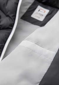 Kviltad svart jacka med vit foder, med dragkedja, kontrasterande innerficka och slät textur. Inre etikett synlig.