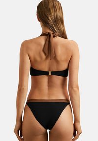 Crni bikini s dizajnom sa vezanjem oko vrata, s smešnim čvorom oko vrata i kontrastnim smešnim pojasom u struku. Glatka tekstura, minimalistički stil.