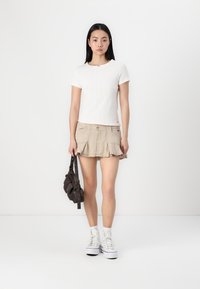 Hvit ribbet kortermet topp kombinert med en beige svingeskjørt, med lommer. Modellen poserer med en mørk håndveske og hvite sneakers.