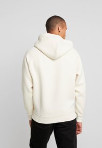 Felpa crema con cappuccio, caratterizzata da maniche raglan e polsini a costine. Texture liscia e vestibilità rilassata, abbinata a pantaloni scuri.