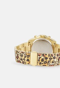 Zlatni sat s remenom s leopard uzorkom, sa stražnjom stranom od nehrđajućeg čelika i kopčom na zakretanje. Kronografski detalj na licu.