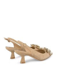 Le décolleté slingback in suede beige presenta una punta affusolata, un tacco basso, decorazioni sul davanti e una fascetta regolabile con un anello metallico.