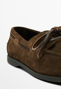 Brune ruskinds loafers med afrundet tå, læder snøre detaljer og sorte accenter på overdelen. Struktureret finish og gummisål.