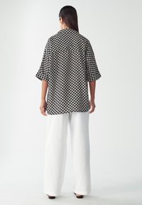 Bílá a černá vzorovaná oversized košile s límečkem, krátkými rukávy, spojená se širokými bílými kalhotami. Hladká tkanina a uvolněný střih.
