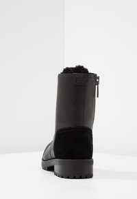 Czarny botek na kostkę wykonany ze skóry i zamszu, z teksturowaną podeszwą, bocznym zamkiem błyskawicznym i miękką podszewką z sztucznego futra.