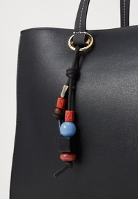 Sort tekstureret læder tote bag med en knude og dekorerende perler i rød, blå og sort, fastgjort til en ring i guldfarvet metal.