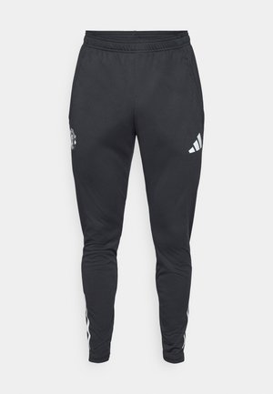 Sorte træningsbukser med elastisk talje, lynlåslommer på siden og hvide Adidas-striber langs siderne. Har et logo på låret.