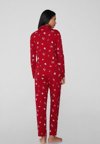 Rode pyjama set met lange mouwen en broek, versierd met een feestelijk patroon van ornamenten en bessen. De stof lijkt zacht en comfortabel te zijn.
