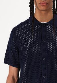 Polo de punto de manga corta en azul marino con un tejido texturizado y un cuello acanalado, que presenta un cierre frontal con botones.