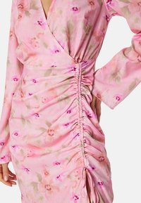 Rosa blommig klänning med långa ärmar, med en wrap-design, rynkning på sidan och ett mjukt, texturerat tyg med en blandning av färger.