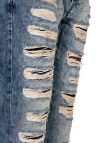 Distressed blue denim jeans with multiple large ripped sections, revealing dark fabric beneath. Frayed edges and varied textures throughout.
