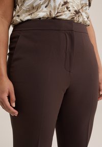 Pantalones elásticos marrones con una textura suave y bolsillos laterales. Diseño de cintura alta, con un frente limpio sin cierres visibles.