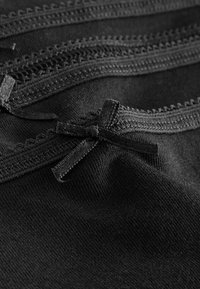 Gros plan sur un tissu noir avec un petit nœud décoratif et une bordure en dentelle festonnée le long du bord.