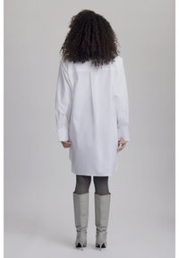 Vestido camisa blanco de mangas largas, con canesú trasero y corte recto. Combinado con botas grises hasta la rodilla. Textura de tela suave.